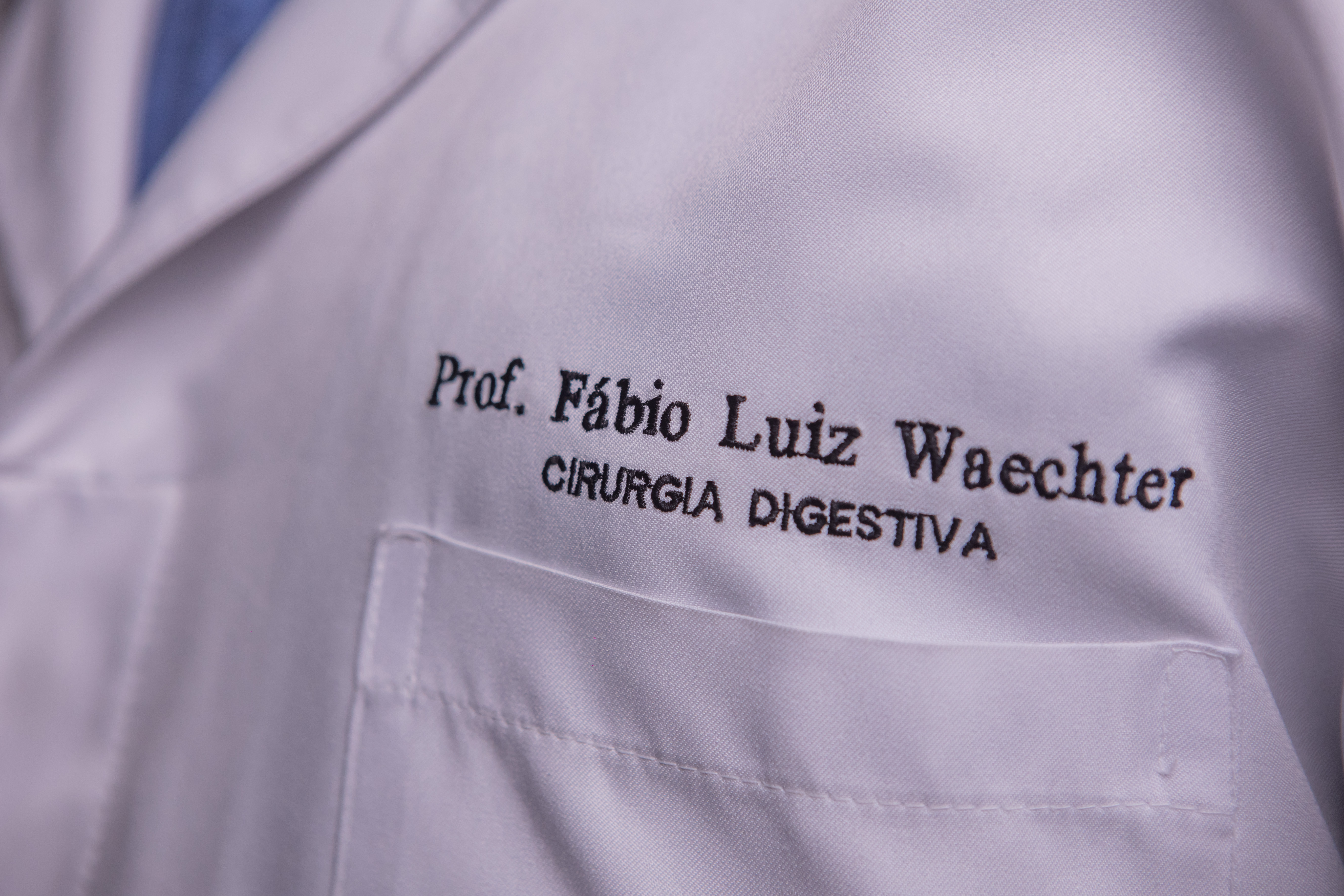 Detalhe do jaleco branco com o nome bordado: Prof. Fábio Luiz Waechter, Cirurgia Digestiva