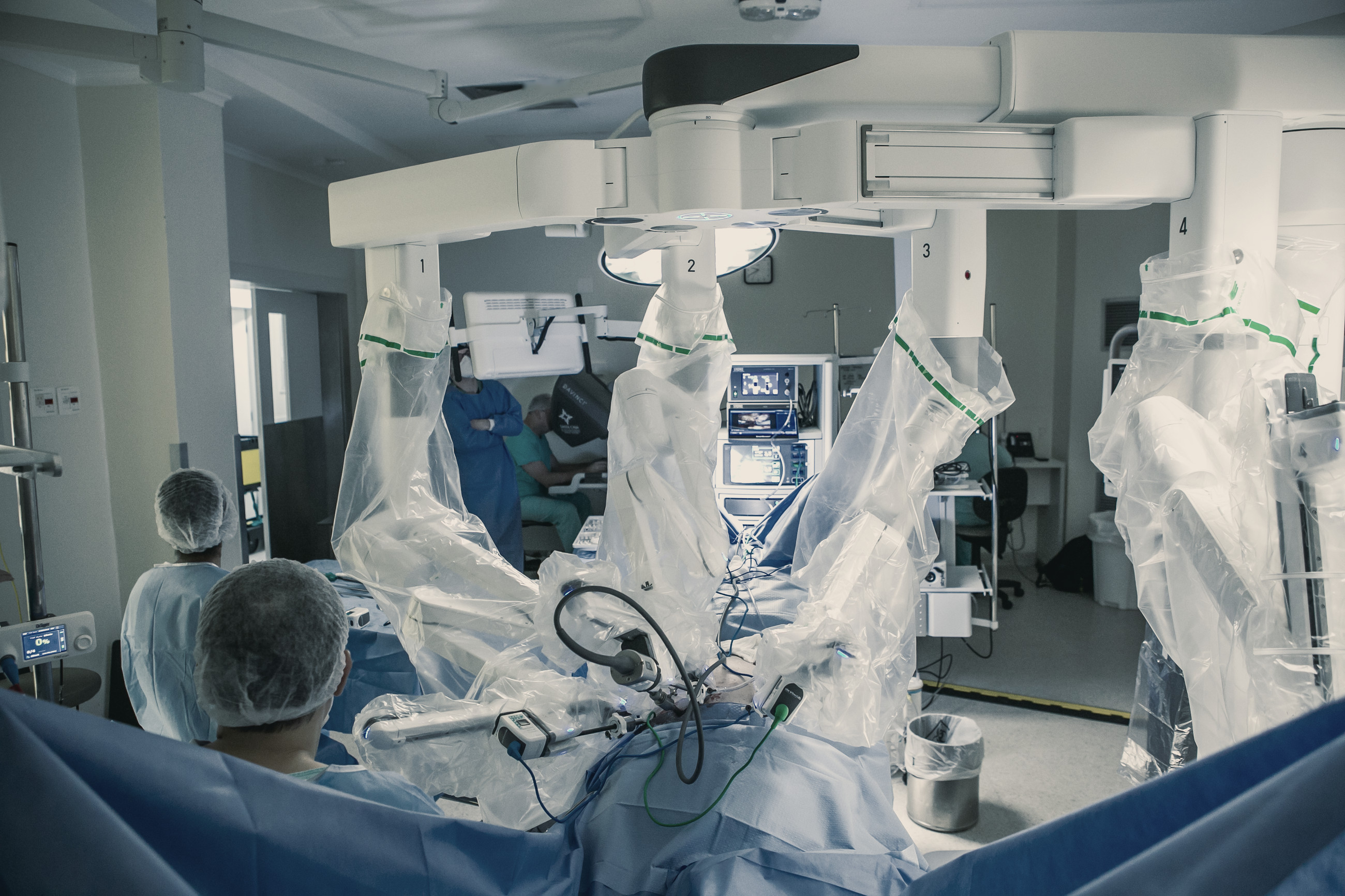 Sala de cirurgia com os braços do robô cobertos por plástico estéril sobre o paciente e a equipe ao redor